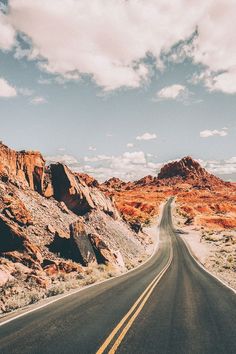 an empty road in the desert with mountains in the background and blue skies above it