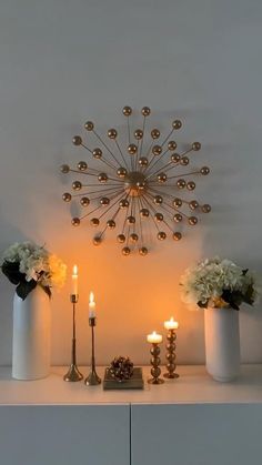 an arrangement of vases with flowers and candles on a table in front of a wall