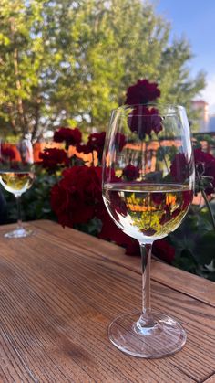 two wine glasses sitting on top of a wooden table next to red and white flowers