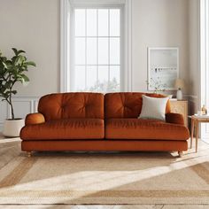 an orange couch sitting in front of a window next to a table with a potted plant