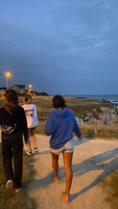 three people walking down a path near the ocean