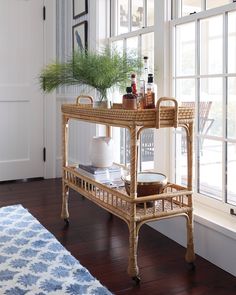 a wicker serving cart with bottles on it in front of a window and rug