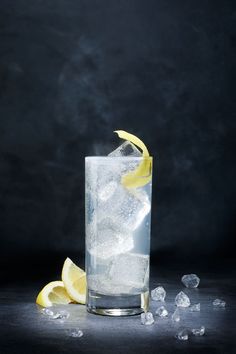 a glass filled with ice and lemon wedges on top of a black tablecloth