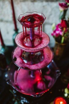 three tiered glass vases with red liquid on them next to candles and flowers