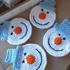 four crocheted snowmen sitting on top of a wooden table