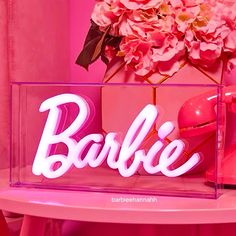 a pink table topped with a vase filled with flowers and baubie letters on top of it