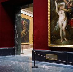 two paintings on display in a museum with red walls and black marble flooring,