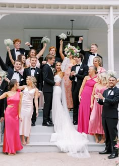 a group of people in formal wear standing on the steps of a house with their arms in the air