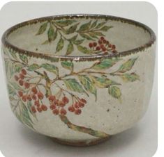 a white bowl with red berries and green leaves on the rim is sitting on a table