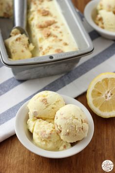 three scoops of ice cream in a white bowl next to lemon slices and a loaf of bread