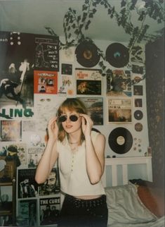 a young woman wearing sunglasses standing in front of a wall covered with records and cds