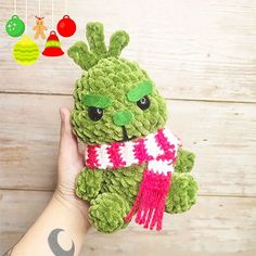 a hand holding a green stuffed animal with a scarf around it's neck and eyes