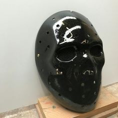 a black mask with holes on it is sitting on a wooden block in front of a white wall