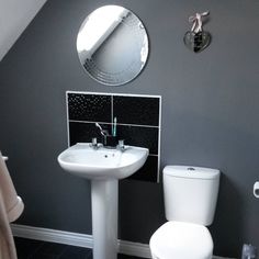 a white toilet sitting next to a sink in a bathroom under a round mirror on the wall