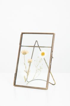 a glass frame with flowers in it sitting on a white table next to a wall