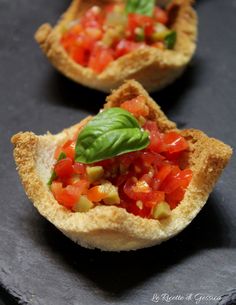 small slices of bread topped with tomatoes and cheese on a wooden cutting board next to other food items