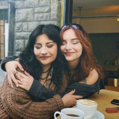 two women hugging each other in front of a table with coffee and doughnuts