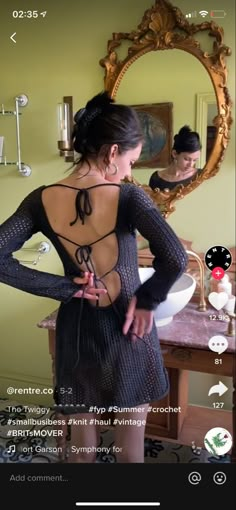 a woman standing in front of a mirror with her back turned to the camera and wearing a black dress