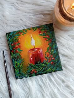 a red candle sitting on top of a white blanket next to a cup and pen