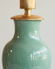 a green vase sitting on top of a wooden table next to a white wall with a gold lid