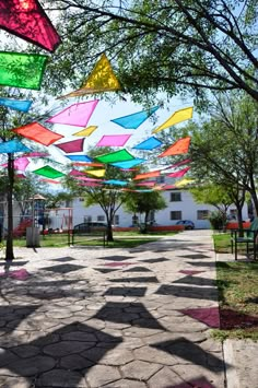 many colorful umbrellas are hanging in the air over a walkway that is lined with trees