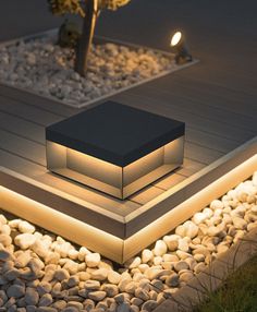 an illuminated box sits on the ground next to some rocks and grass in front of it