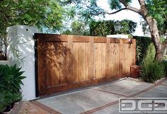 a large wooden gate in front of a white wall and some plants on the sidewalk