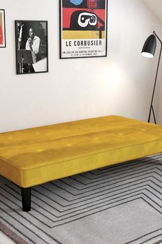 a yellow bed sitting on top of a rug next to a wall with pictures above it