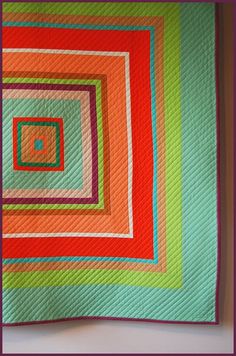 a quilted wall hanging with an orange and green square on it's side