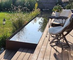 a table and chairs on a wooden deck next to a small pond with water in it