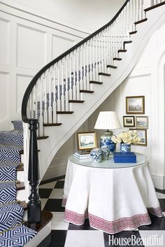 a white table topped with a lamp next to a stair case and pictures on the wall