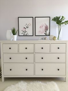 a white dresser with two pictures on the wall above it and plants in vases