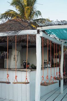 an outdoor bar with swings and palm trees in the backgrouds, on a wooden deck