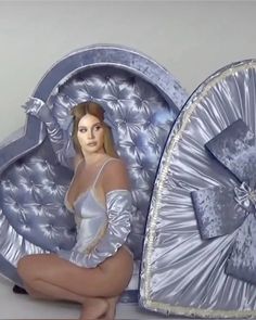 a woman is sitting in front of a heart shaped bed with silver sheets on it