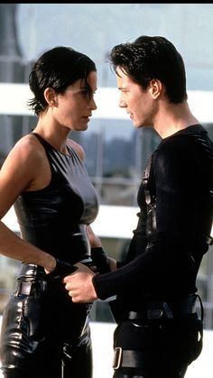 two people standing next to each other wearing black leather outfits and holding hands on their hips