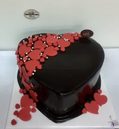 a heart shaped cake with red hearts on it's side and black frosting