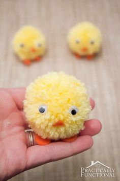 a hand holding a small yellow stuffed animal with eyes on it's face and three smaller ones in the background