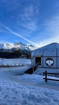 a small white building sitting in the middle of a snow covered field with mountains in the background