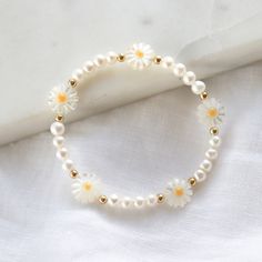 a white bracelet with daisies and pearls on the clasp is laying on a white cloth