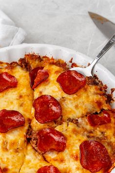 a pepperoni pizza in a white dish with a serving utensil next to it