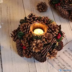 a candle that is sitting next to some pine cones and music sheets on a table