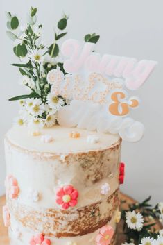 a white cake with flowers on top and a happy birthday sign in the middle is sitting on a wooden table