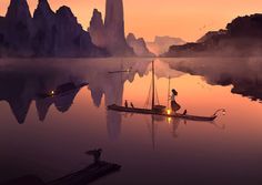 a woman sitting in a boat on top of a lake next to mountains and birds