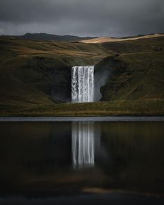 an image of a waterfall that is in the middle of some water with dark clouds above it