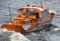 a small wooden boat in the water with people on it's deck and steering wheel