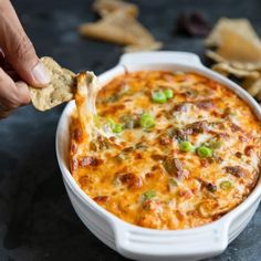 a hand dipping a cracker into a casserole with cheese and green onions