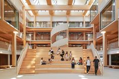 several people are walking up and down the stairs in a large building with wooden floors