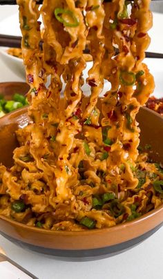 a bowl filled with noodles and vegetables on top of a table next to chopsticks