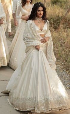 two women in white gowns walking down a path with one woman wearing a long dress