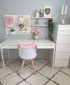 a white desk sitting on top of a rug next to a shelf filled with flowers